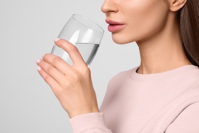 Healthy habit. Woman drinking fresh water from glass on light grey background, closeup