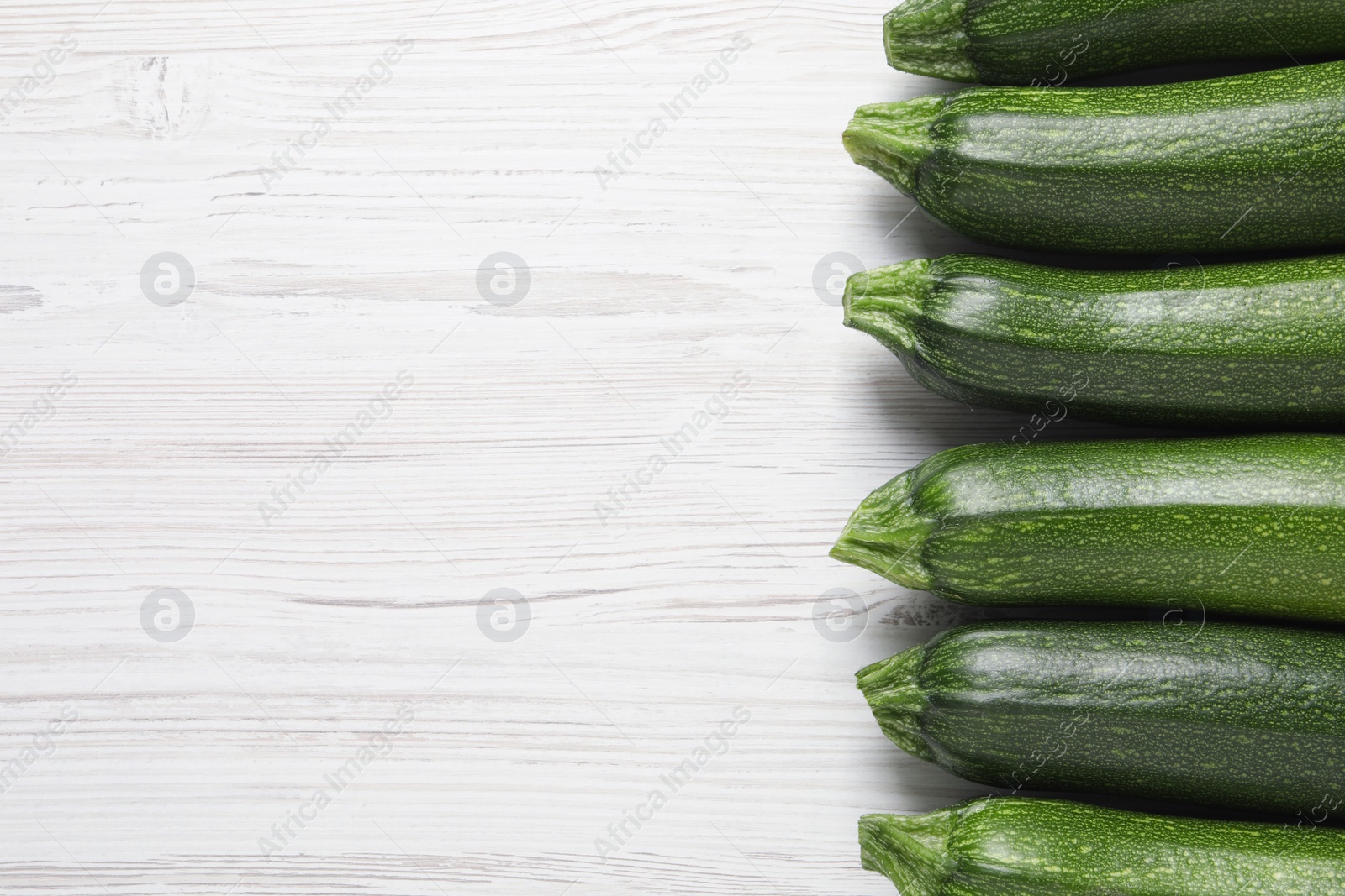 Photo of Raw ripe zucchinis on white wooden table, flat lay. Space for text