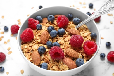 Photo of Tasty homemade granola with berries on white marble table, closeup. Healthy breakfast