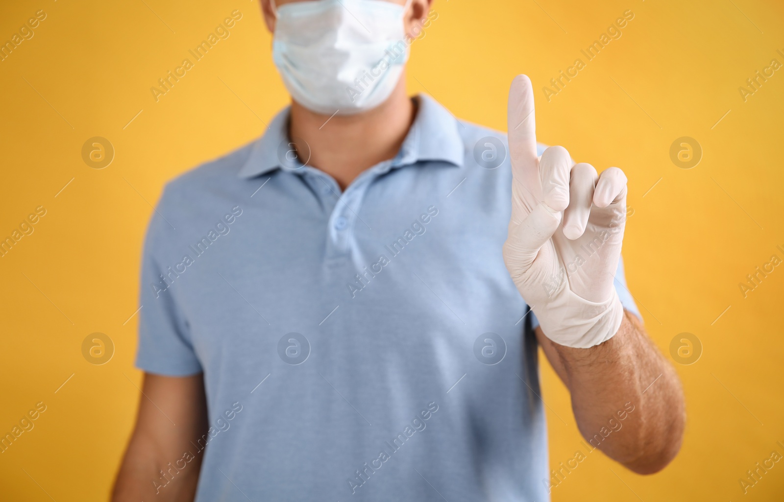 Photo of Man in protective face mask and medical gloves with raised index finger on yellow background, closeup