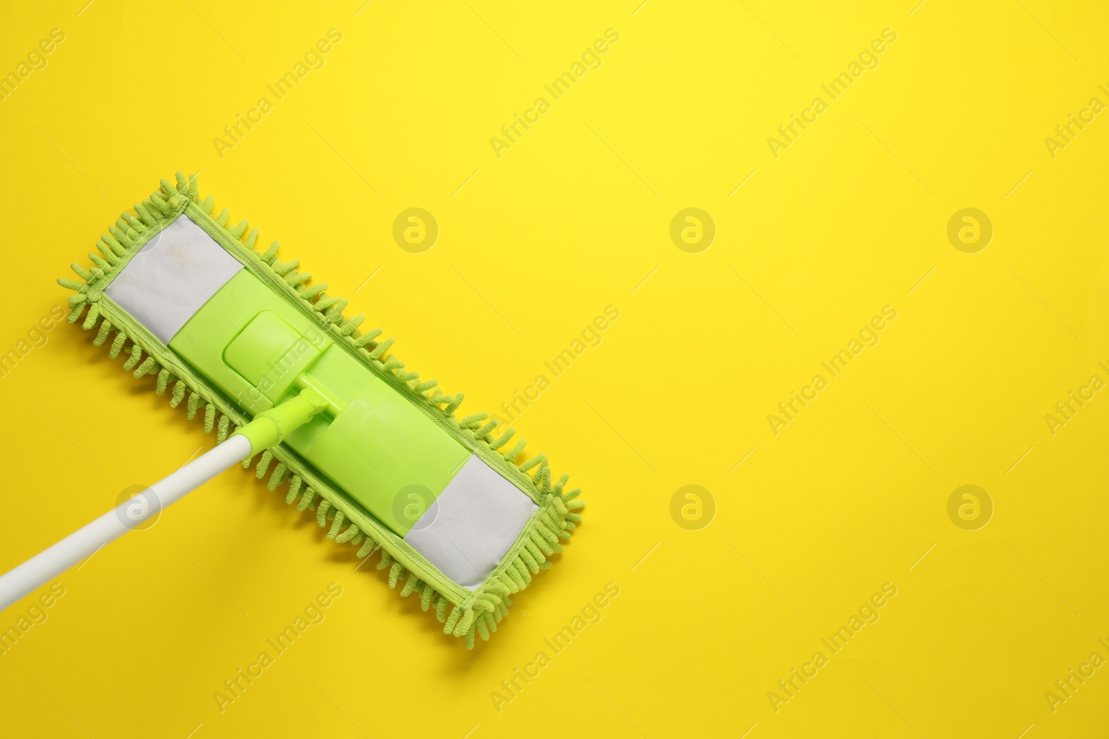 Photo of Mop with plastic handle on yellow background, top view. Space for text