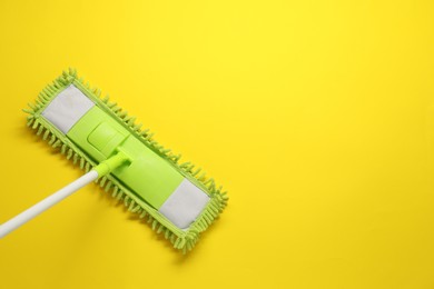 Mop with plastic handle on yellow background, top view. Space for text