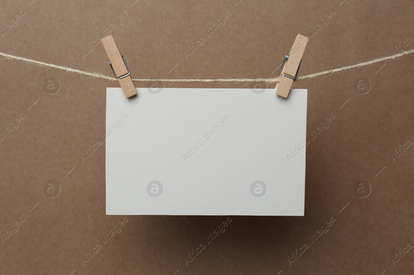 Photo of Wooden clothespins with blank notepaper on twine against brown background. Space for text