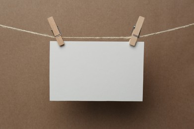 Wooden clothespins with blank notepaper on twine against brown background. Space for text