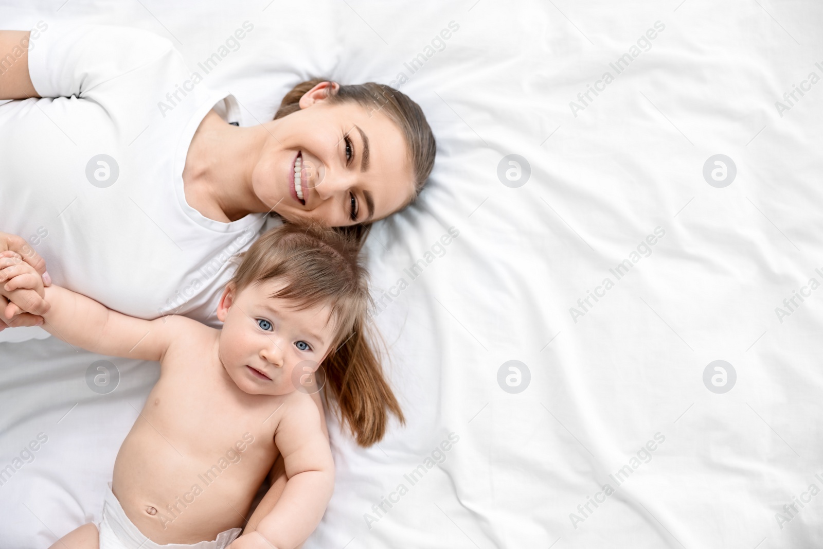 Photo of Family portrait of happy mother with her baby on bed, top view. Space for text