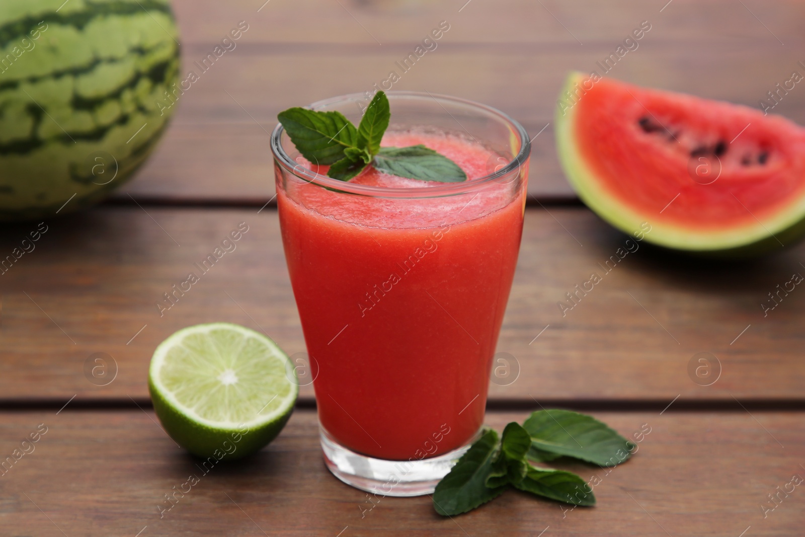 Photo of Glass of delicious watermelon smoothie with mint and lime on wooden table