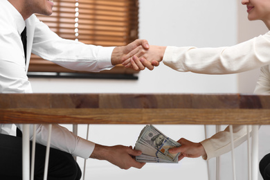 Photo of Woman shaking hands with man and giving bribe under table in office, closeup
