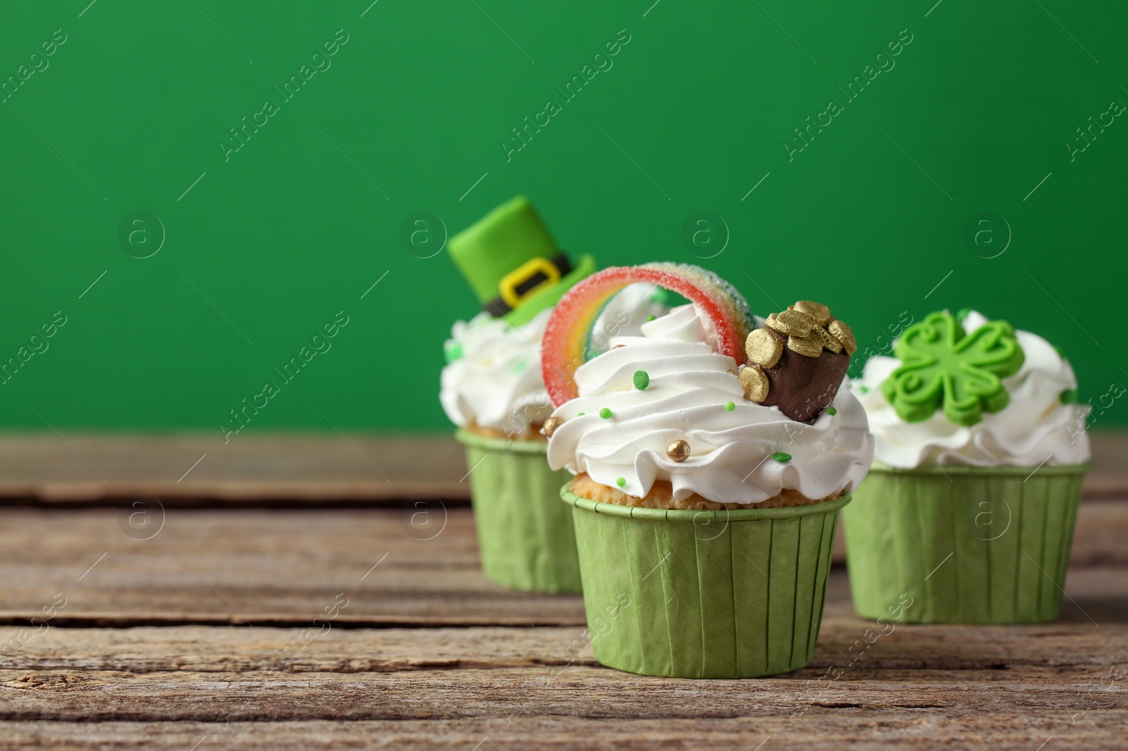 Photo of St. Patrick's day party. Tasty festively decorated cupcakes on wooden table, closeup. Space for text