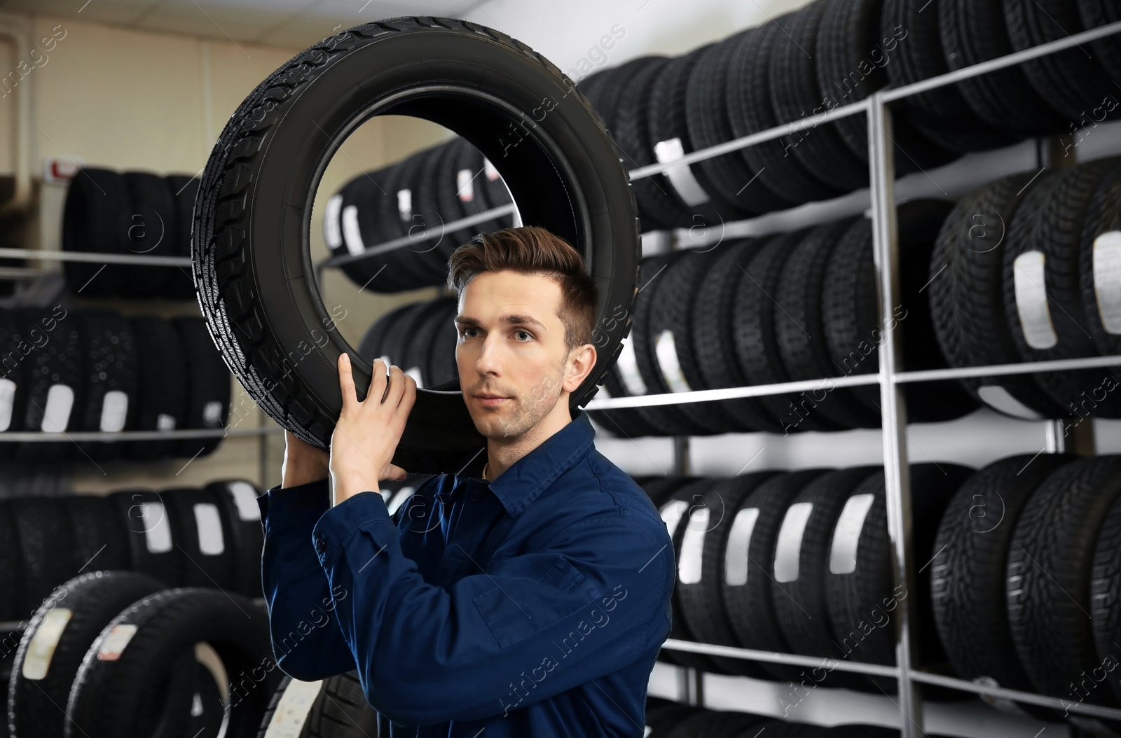 Photo of Young male mechanic with car tire in automobile service center