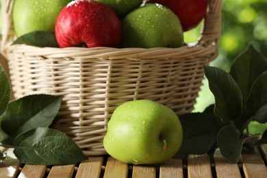 Different ripe apples with water drops and green leaves on wooden table outdoors, closeup