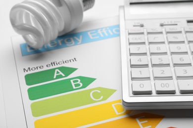 Photo of Energy efficiency rating chart, fluorescent light bulb and calculator, closeup