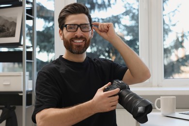Photo of Professional photographer in glasses holding digital camera at table indoors