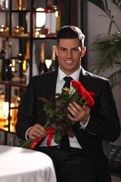 Happy man with roses waiting for his girlfriend in restaurant on Valentine's day