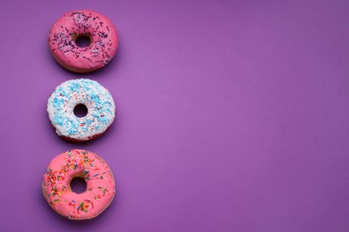 Sweet glazed donuts decorated with sprinkles on purple background, flat lay and space for text. Tasty confectionery