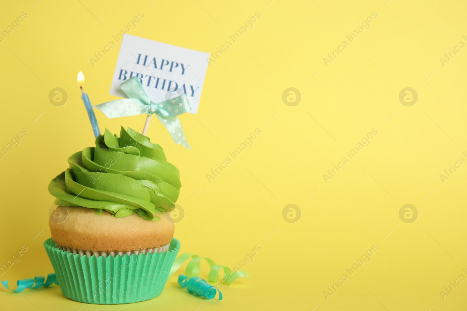 Photo of Beautiful birthday cupcake and streamers on yellow background. Space for text