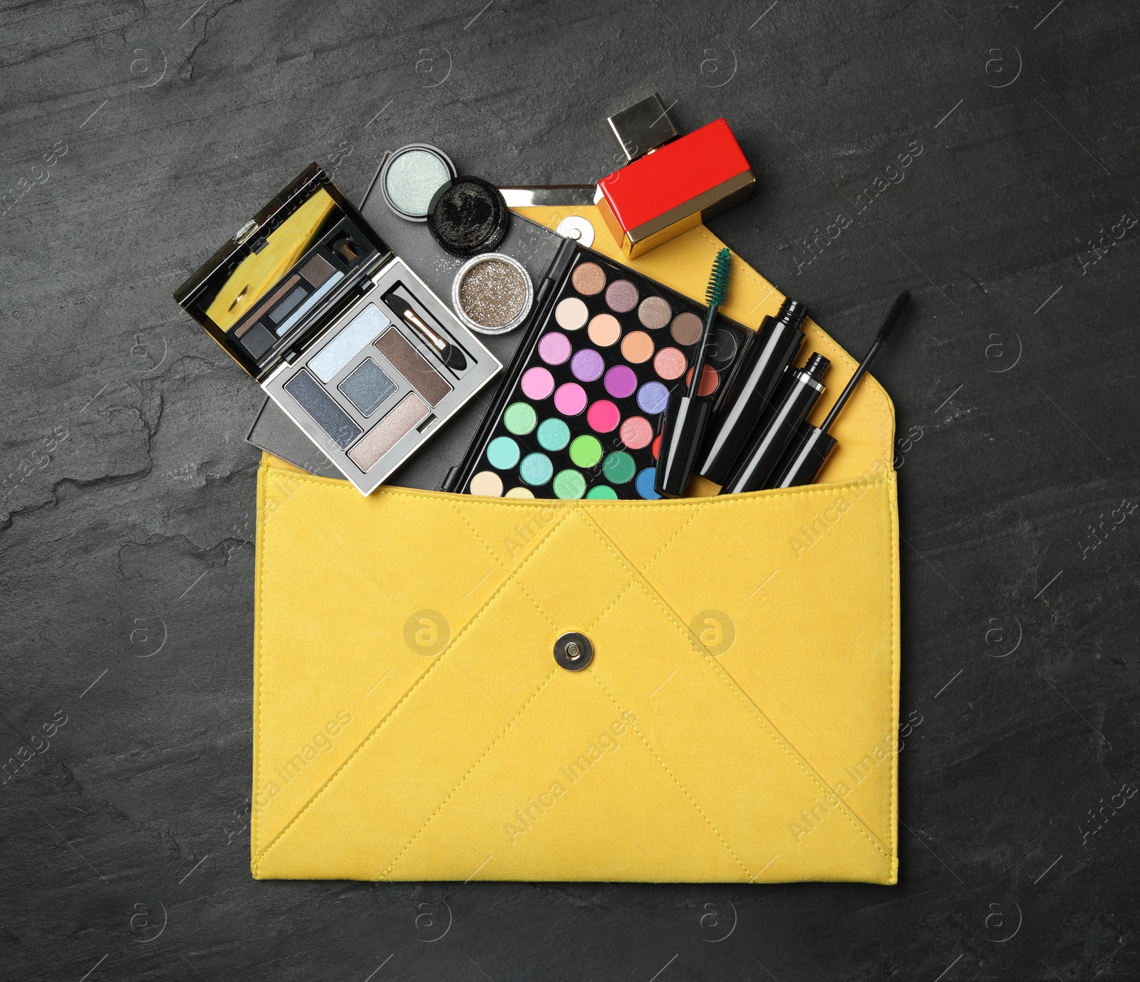 Photo of Cosmetic bag with makeup products on black slate background, flat lay