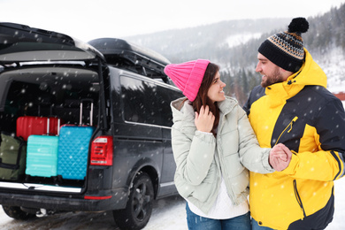 Happy couple near car with open trunk on snowy road. Winter vacation