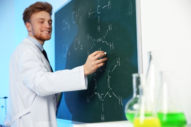 Male scientist writing chemical formula on chalkboard indoors