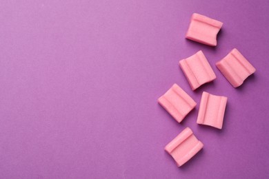 Photo of Tasty pink chewing gums on purple background, flat lay. Space for text