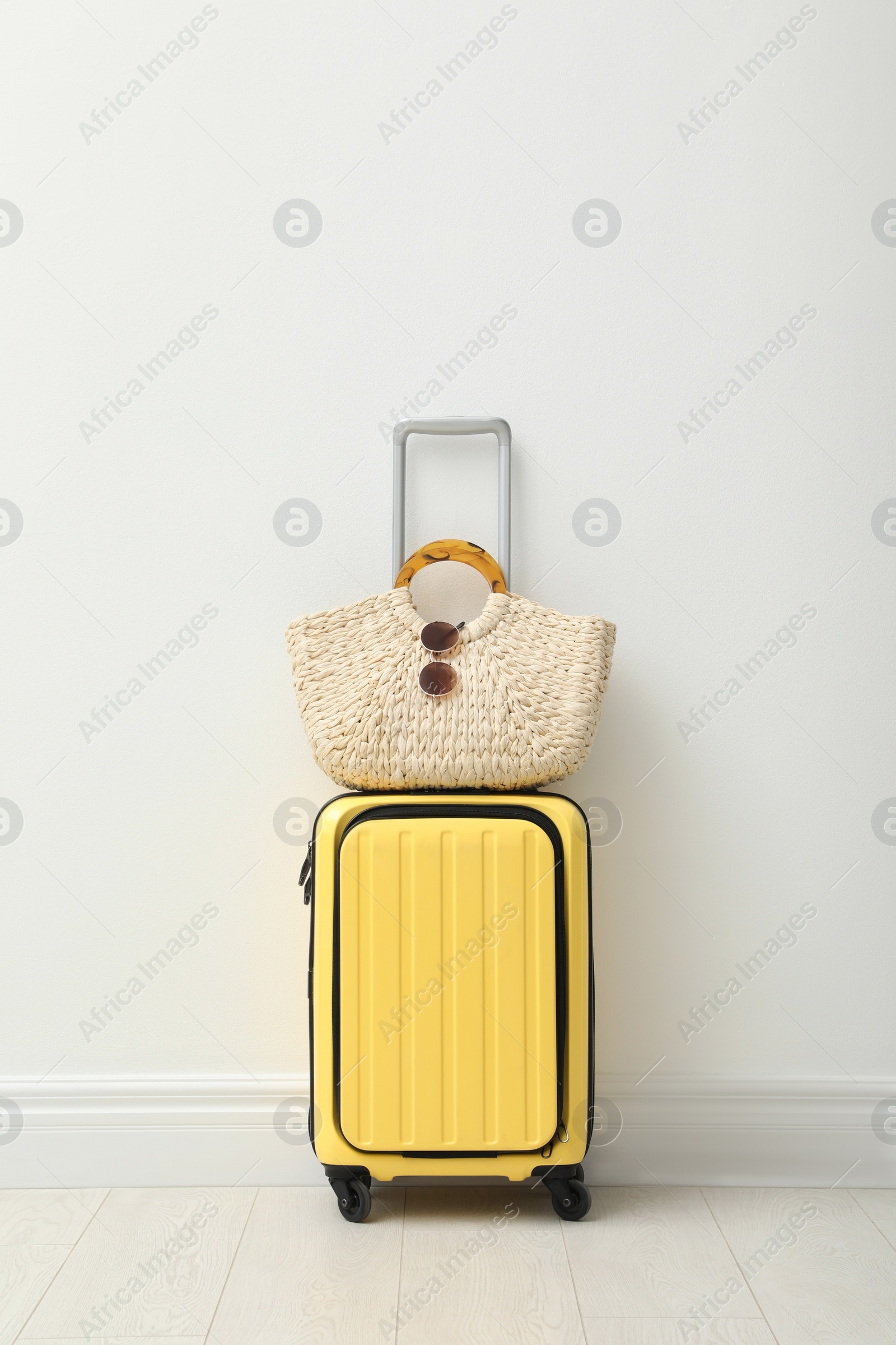 Photo of Suitcase packed for trip and summer accessories near white wall indoors