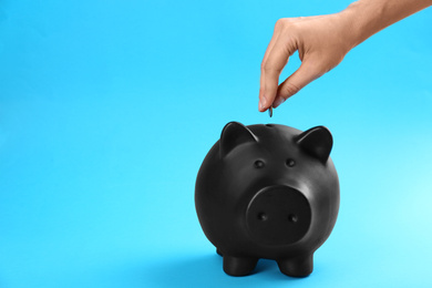 Woman putting coin into piggy bank on blue background, closeup