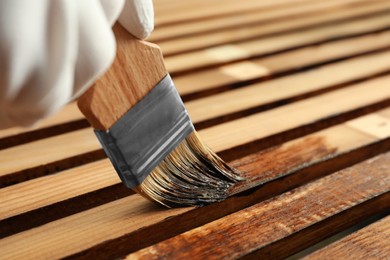 Photo of Worker applying wood stain onto planks, closeup