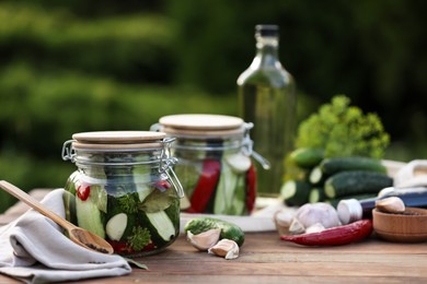 Photo of Jars of delicious pickled cucumbers and ingredients on wooden table against blurred background. Space for text