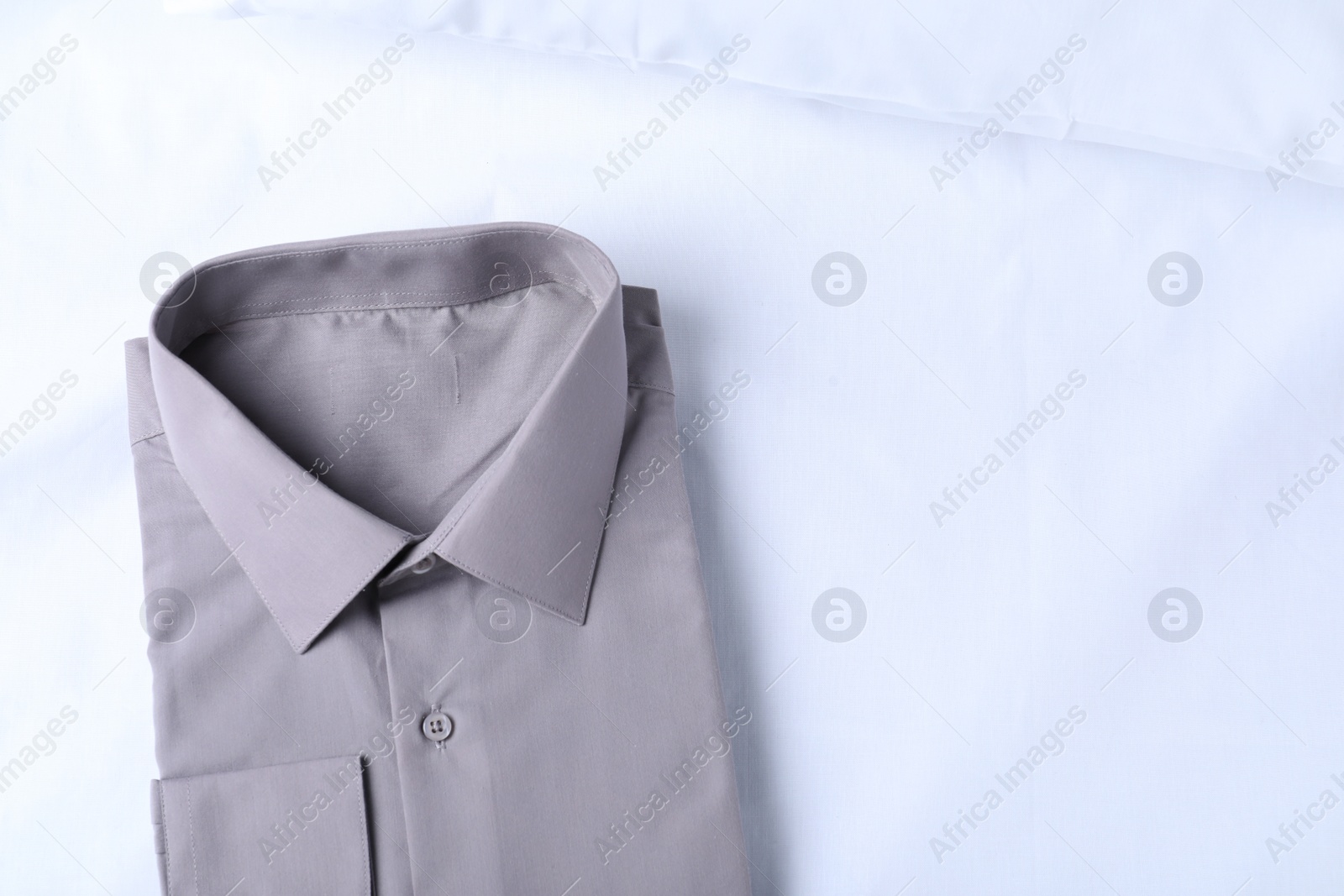 Photo of Stylish grey shirt on white fabric, top view with space for text. Dry-cleaning service