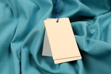 Blank white tags on light blue fabric, closeup. Space for text