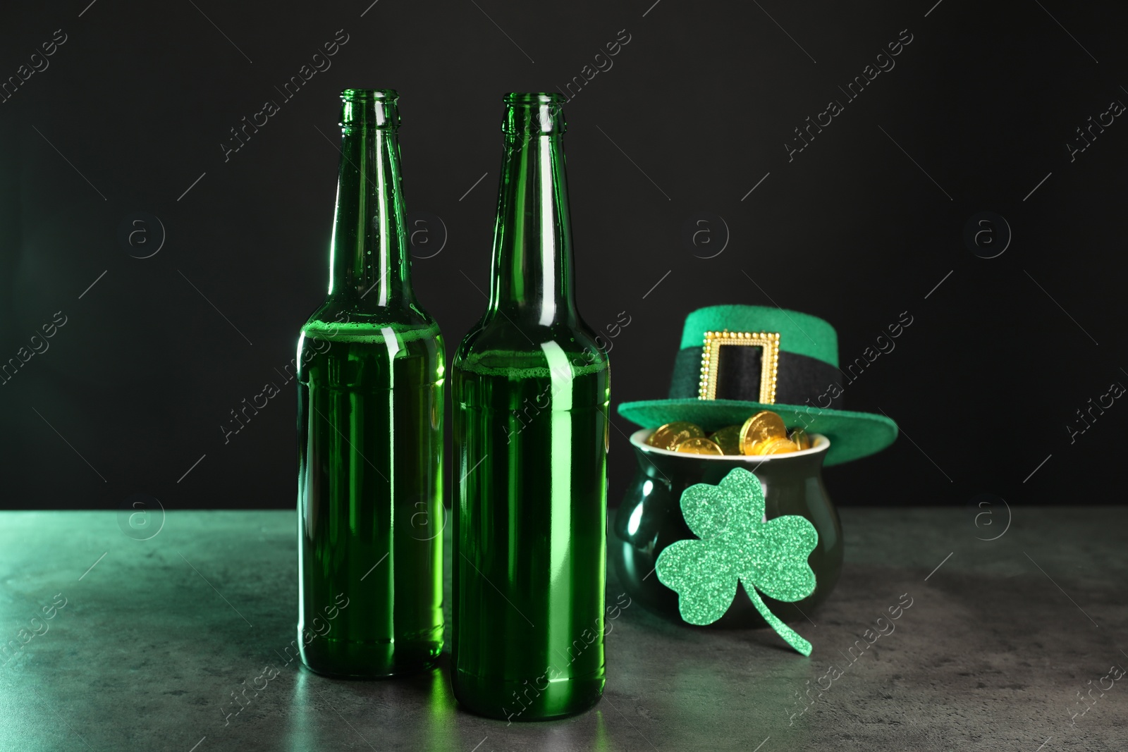 Photo of St. Patrick's day celebration. Beer in green bottles, leprechaun hat, pot of gold and decorative clover leaf on grey table