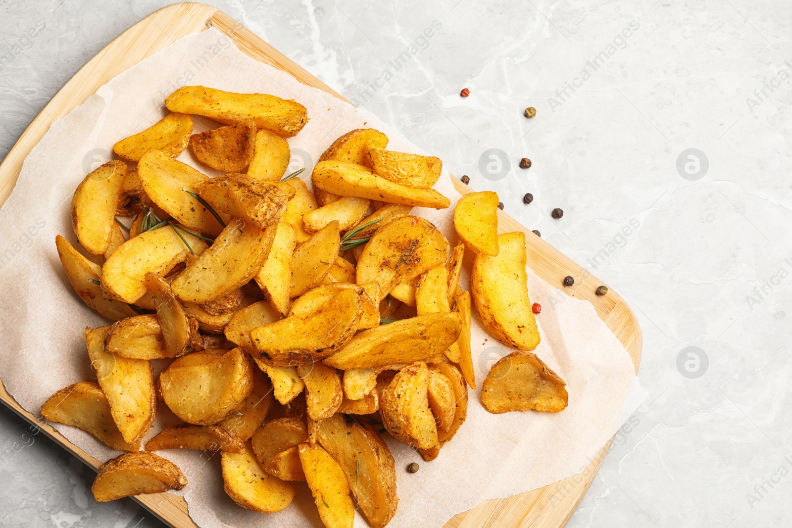 Photo of Board with delicious oven baked potatoes on marble background, top view