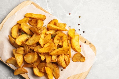 Photo of Board with delicious oven baked potatoes on marble background, top view