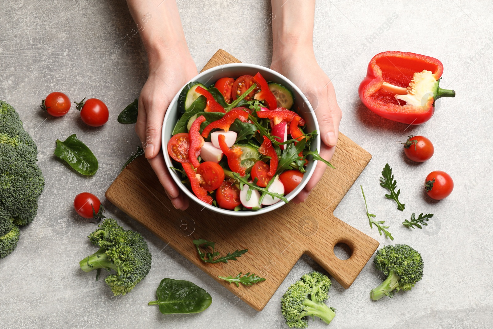 Photo of Woman with tasty fresh vegetarian salad at light grey table, top view