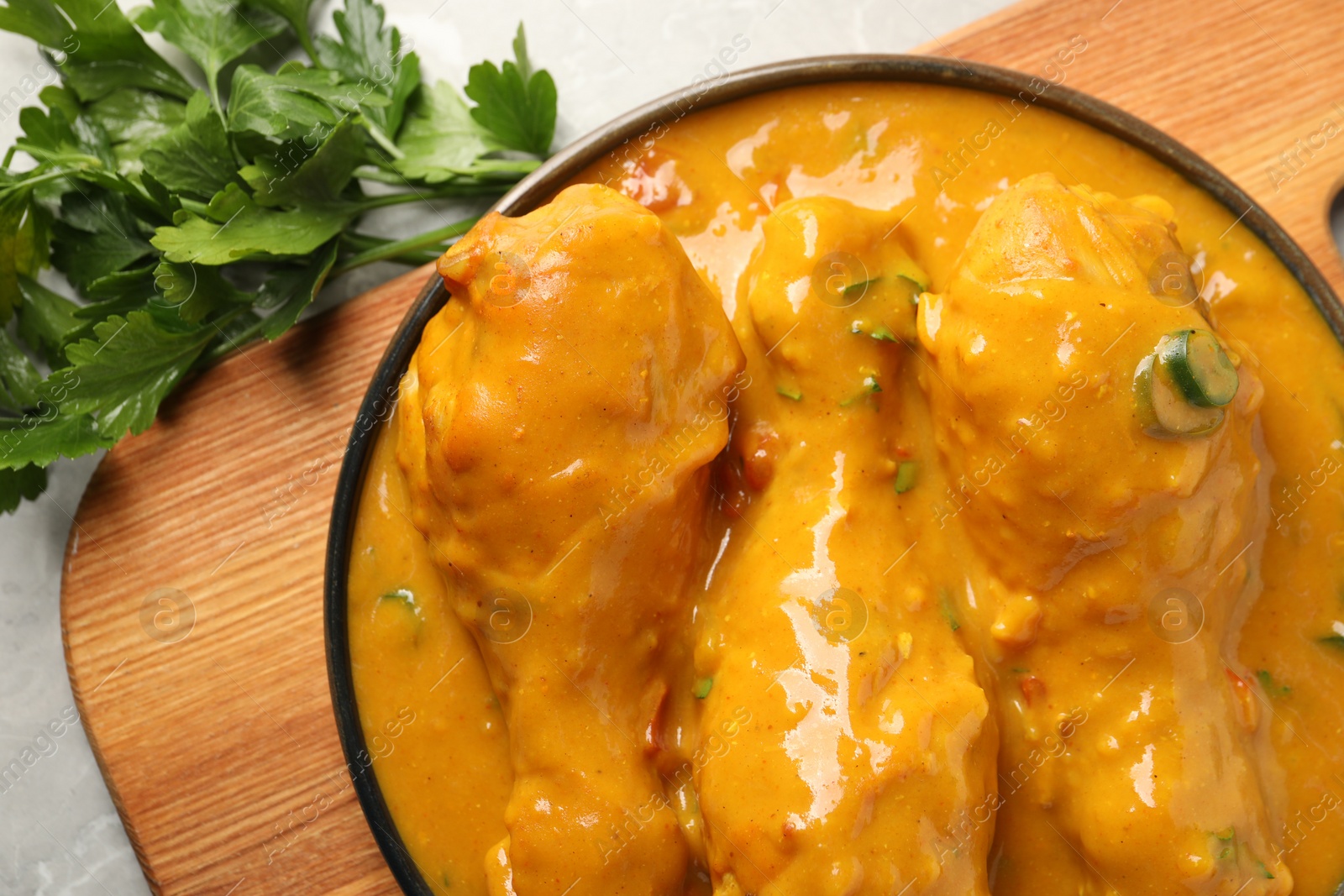 Photo of Tasty chicken curry and parsley on grey textured table, flat lay