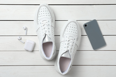 Pair of stylish shoes, modern smartphone and wireless earphones on white wooden table, flat lay