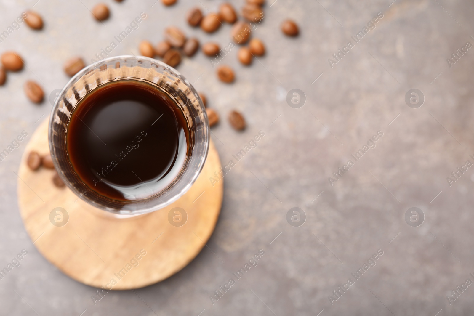 Photo of Shot glass with coffee liqueur and beans on light grey table, top view. Space for text