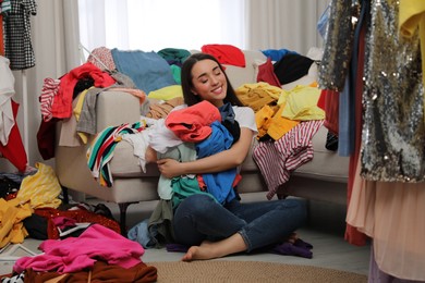 Photo of Happy young woman with lots of clothes in room. Fast fashion