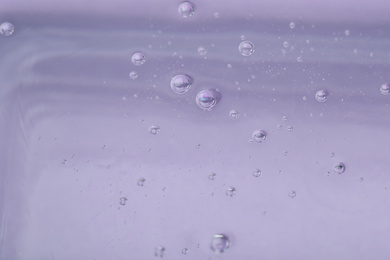 Pure transparent cosmetic gel on lilac background, closeup