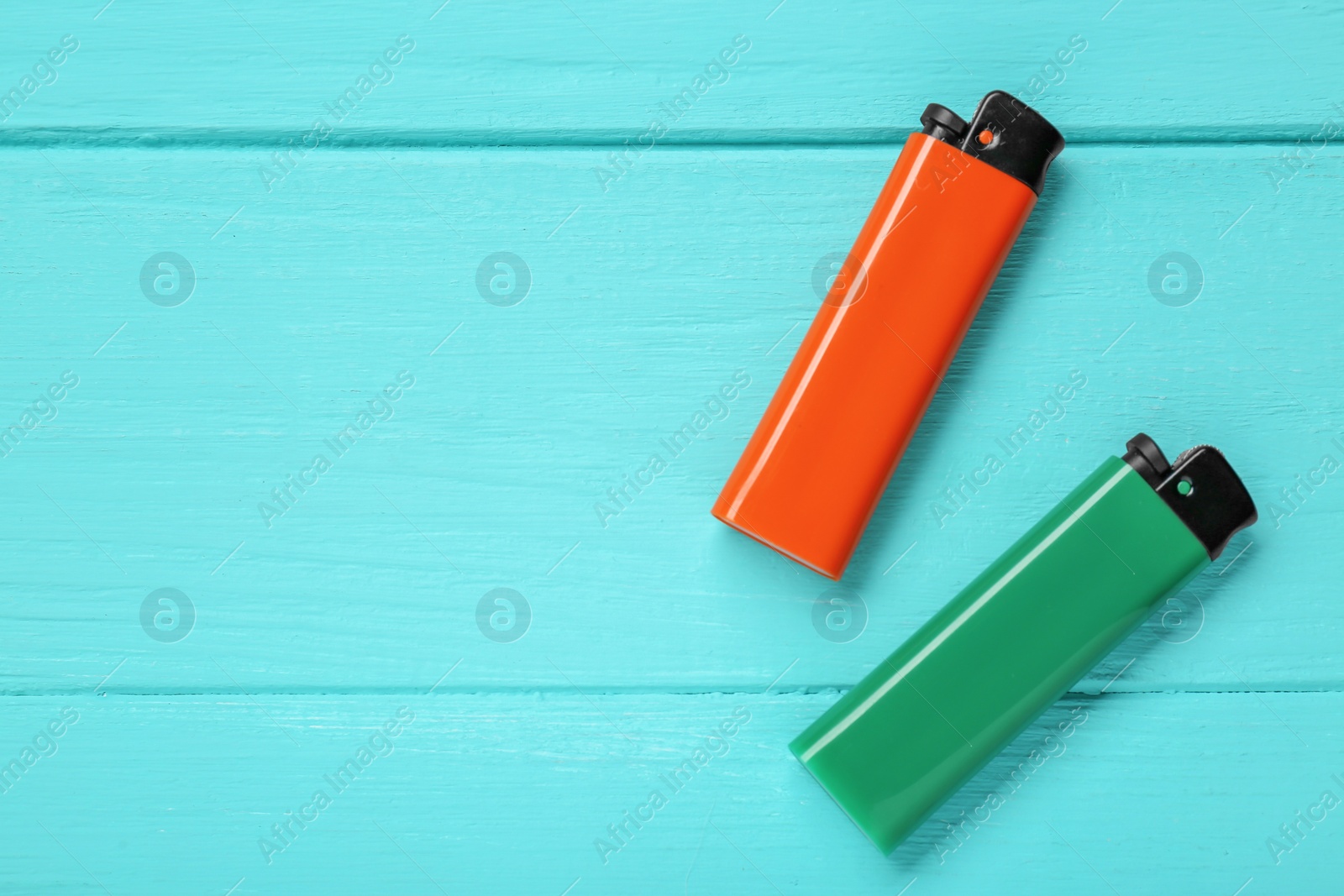 Photo of Stylish small pocket lighters on turquoise wooden background, flat lay. Space for text