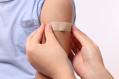 Woman sticking plaster on boy's arm after vaccination against white background, closeup