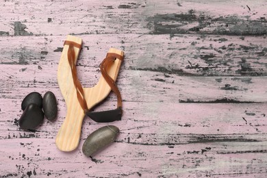 Photo of Slingshot with stones on old pink wooden background, flat lay. Space for text