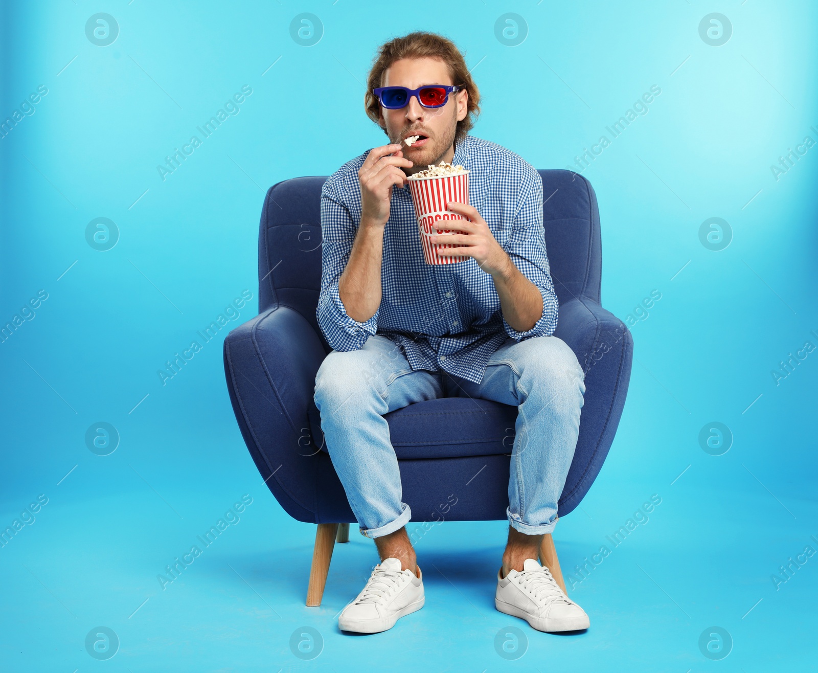 Photo of Emotional man with 3D glasses and popcorn sitting in armchair during cinema show on color background