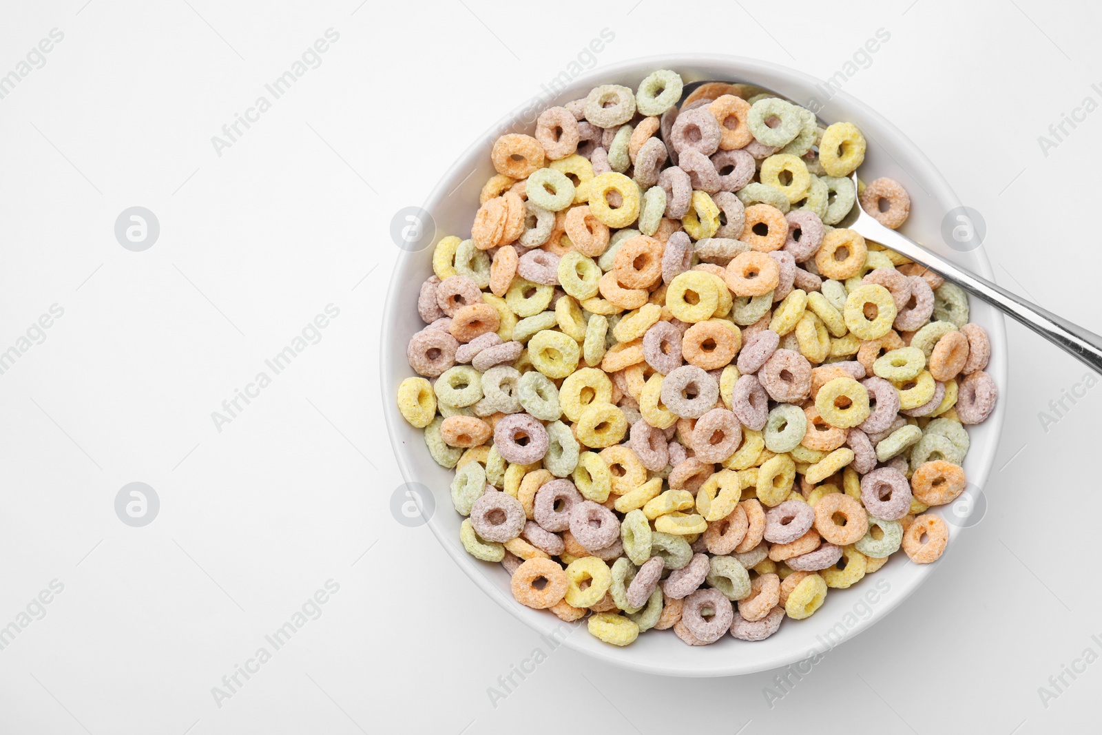 Photo of Tasty cereal rings in bowl and spoon on white table, top view. Space for text