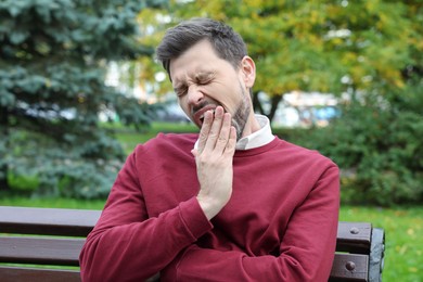 Photo of Sleepy tired man yawning on bench in beautiful green park