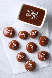 Tasty candies, caramel sauce and salt on light grey table, top view