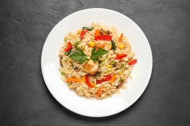 Photo of Delicious rice pilaf with chicken and vegetables on black table, top view