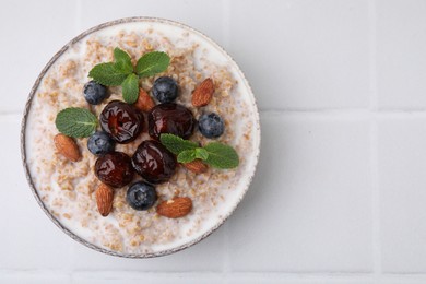 Photo of Tasty wheat porridge with milk, dates, blueberries and almonds in bowl on white table, top view. Space for text