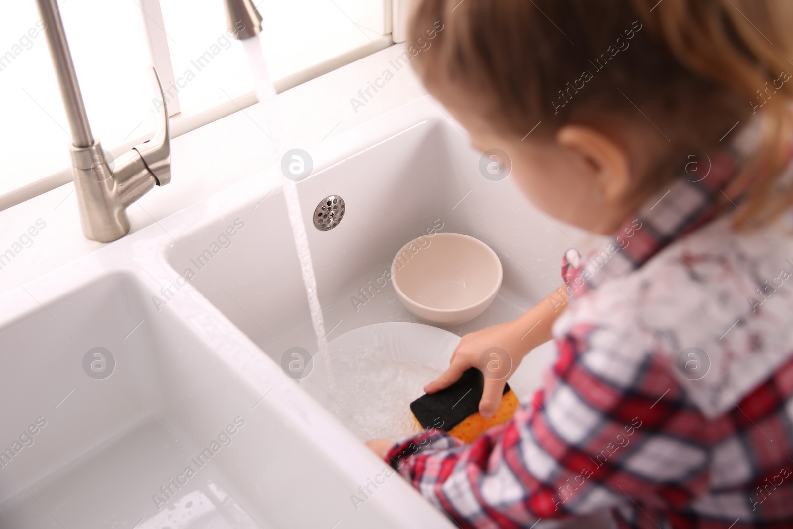Photo of Little girl washing dishes in kitchen at home, closeup