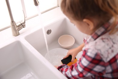 Photo of Little girl washing dishes in kitchen at home, closeup