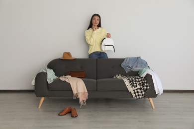 Photo of Young woman holding backpack near sofa with clothes indoors